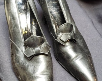 May include: Pair of black leather pointed-toe shoes with a small bow detail on the vamp.