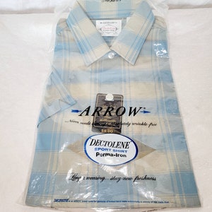 May include: A new, unworn Arrow Dectolene sport shirt in a clear plastic package. The shirt has a plaid pattern in light blue and beige. The packaging includes the Arrow logo and text that reads "Never needs absolutely wrinkle-free."