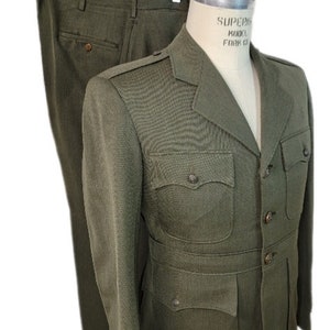 May include: A green military uniform suit with a jacket and pants. The jacket has a button closure, four pockets, and a collar. The pants have a zipper and button closure.