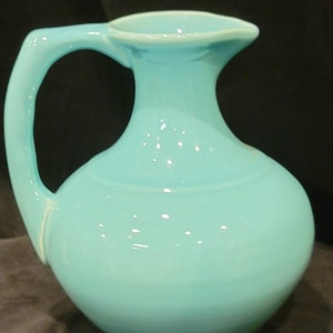 May include: A turquoise ceramic pitcher with a rounded body and a flared spout. The pitcher has a simple, elegant design.