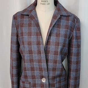 May include: A plaid blazer in shades of blue and burgundy, displayed on a mannequin. The jacket features a classic notched collar, two front pockets, and two button closure. The fabric has a subtle texture.