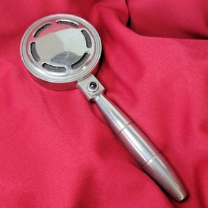 May include: A silver microphone with a round head and a long handle. The microphone has a black button on the side.
