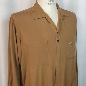 May include: A brown long-sleeved button-down shirt with a collar and a pocket on the left side. The shirt has a gold logo on the right side and the text "SUPERIOR MODEL FORM CO" on the collar.