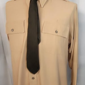 May include: A tan long-sleeve shirt with a black tie. The shirt has two large pockets on the front and the text "SUPERIOR MODEL FORK CO" on the collar.