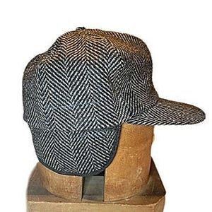 May include: A black and white herringbone patterned wool cap with ear flaps. The cap is on a wooden display stand.
