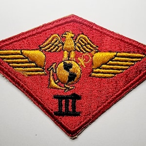 May include: A red diamond-shaped patch with gold embroidered wings, a globe with an anchor, and the number "III" in black.