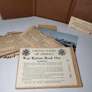 May include: A vintage, tan-colored, United States War Ration Book One with a warning about penalties for violating rationing orders and regulations. The book has a seal of the United States of America and the text "Office of Price Administration".