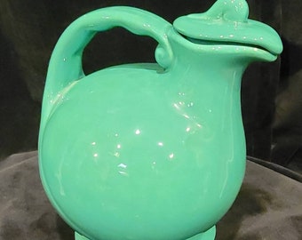 May include: A teal ceramic pitcher with a lid and a curved handle. The pitcher has a rounded body and a wide base.