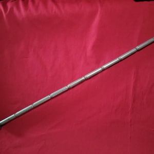 May include: A silver-colored, segmented antenna with a pointed tip and a rounded base. The antenna is lying diagonally on a red background. The antenna appears to be made of metal.