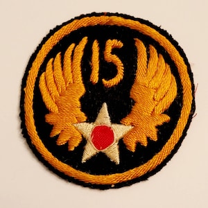 May include: A black and gold embroidered patch with a white star and red center. The number "15" is embroidered in yellow above the star. The patch has a gold border.