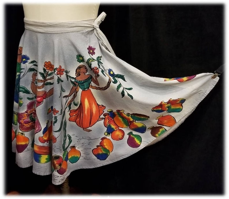 May include: A white wrap skirt with a colorful print of people, flowers, and pottery. The skirt has a tie closure at the waist.
