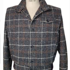 May include: A gray, brown, and white plaid jacket with a button-up front and a single pocket on the left chest. The jacket has a label that reads "Superior Model Form Co."