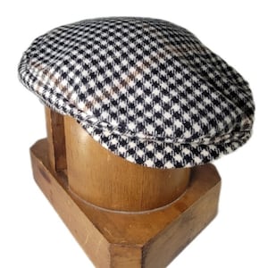 May include: A black, white, and brown checkered wool newsboy cap on a wooden hat form.