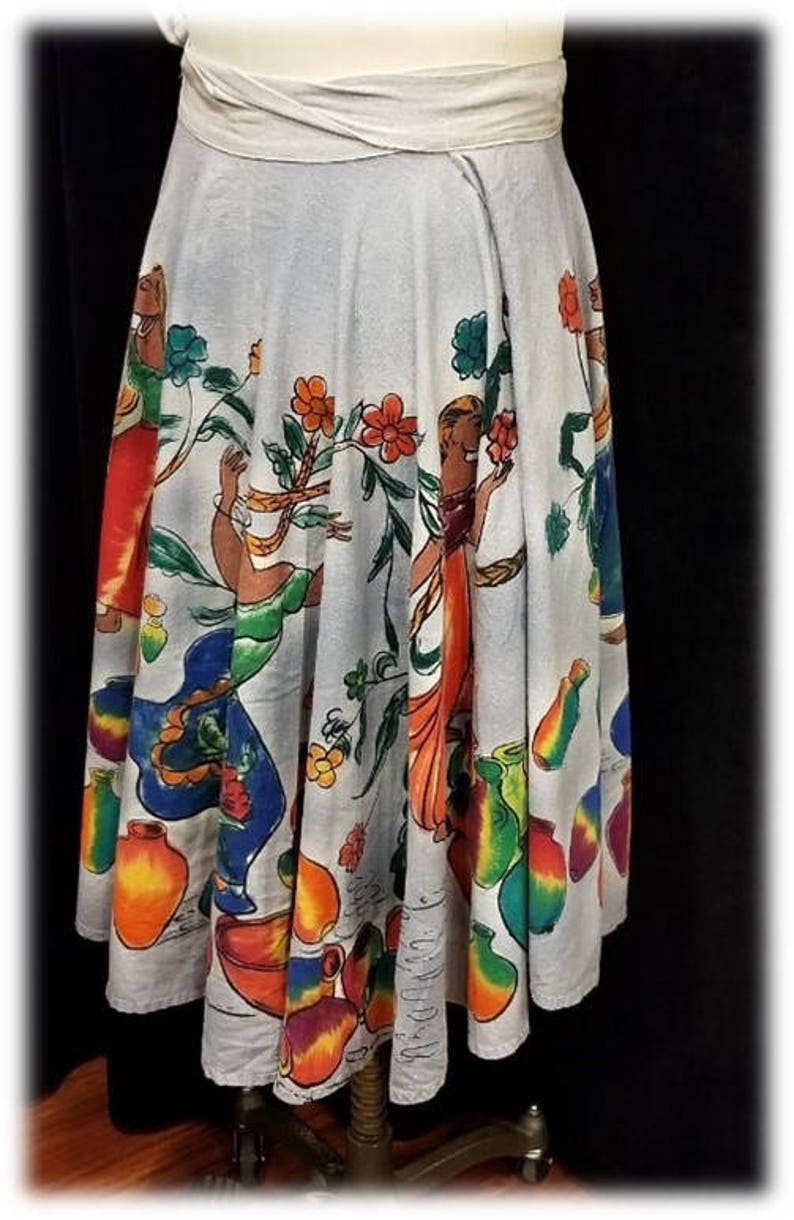 May include: A white cotton skirt with a colorful print of women and flowers. The skirt has a wide waistband and a full, flowing silhouette.