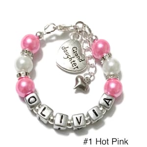 May include: A pink and white beaded bracelet with a silver charm that says "Grand daughter". The bracelet also has silver beads that spell out the name "Olivia".