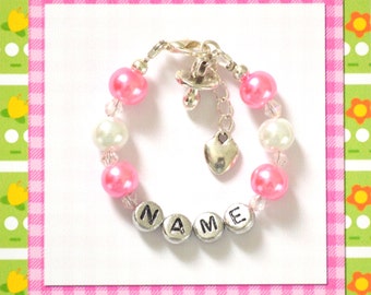 May include: A pink and white beaded bracelet with a silver charm of a pacifier and a heart. The bracelet has silver beads that spell out the word "NAME".