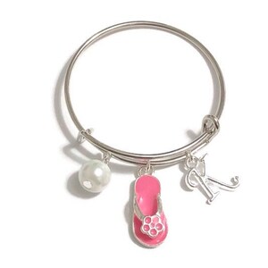 May include: Silver-tone adjustable bangle bracelet with a pink flip-flop charm, a white pearl bead, and a silver letter "R" charm. The flip-flop charm has a white flower design. The bracelet is on a white background.