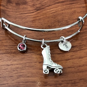 May include: A silver charm bracelet with a roller skate charm, a pink crystal charm, and a charm with the letter "T" engraved on it.