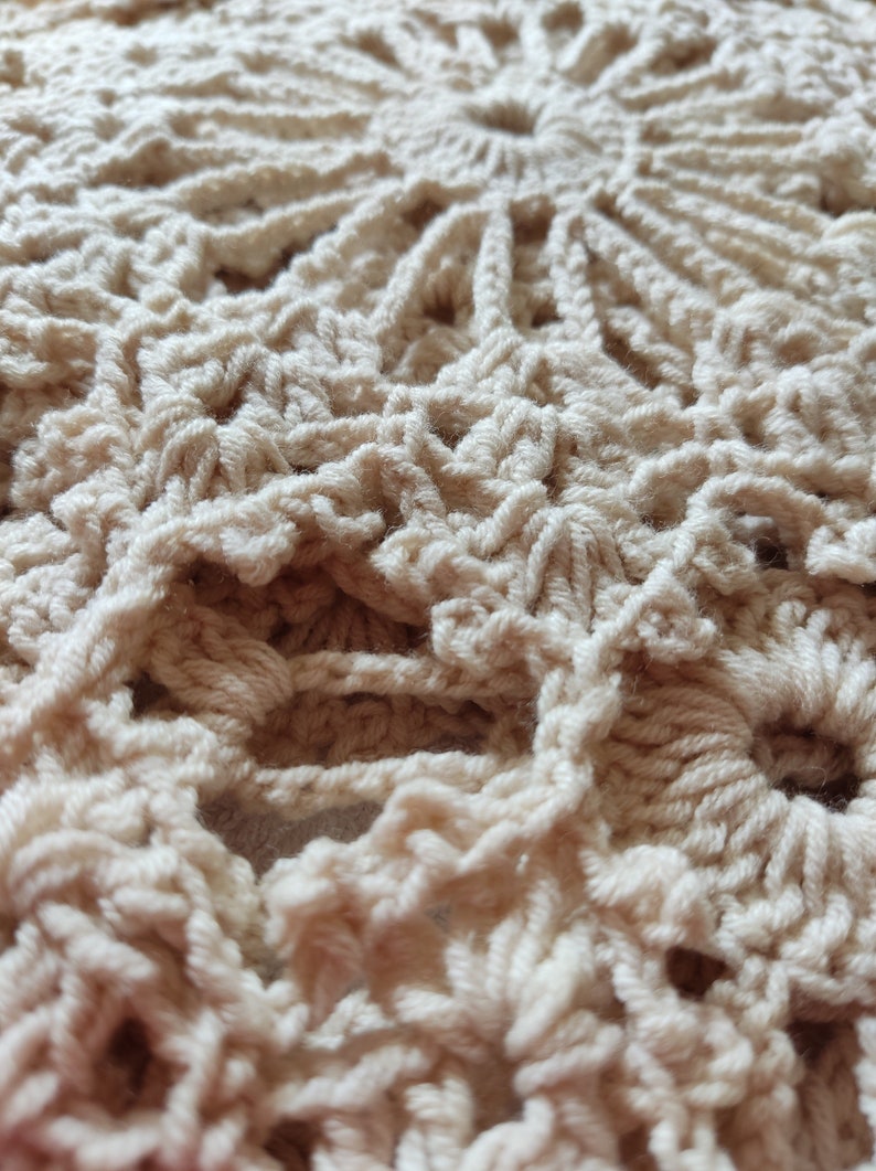 May include: Close-up of a cream-colored, crocheted doily. The handmade piece features a circular design with intricate patterns and openwork details. The texture of the yarn is visible, creating a soft and inviting aesthetic. The doily is likely used for home decor.