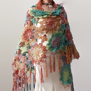 May include: A colorful crochet shawl with a floral pattern and fringe. The shawl is made in shades of green, blue, orange, and pink.