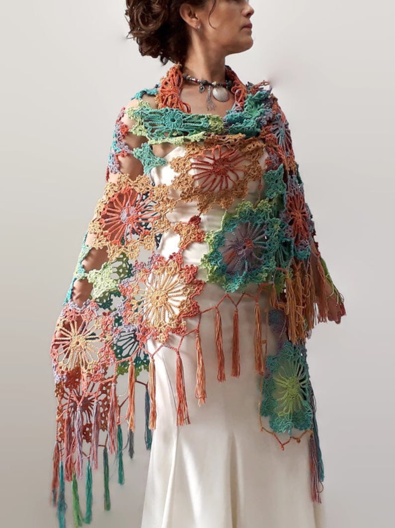 May include: A colorful crochet shawl with a floral pattern and fringe. The shawl is made in shades of green, blue, orange, and pink.