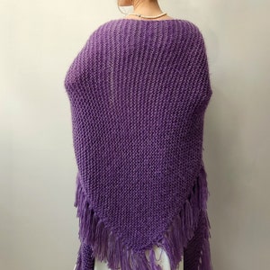 May include: A purple knitted shawl with fringe. The shawl is made of a soft, fuzzy yarn and has a triangular shape.