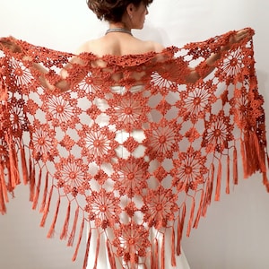 May include: A terracotta crocheted shawl with a fringed border. The shawl is made with a delicate, openwork pattern.
