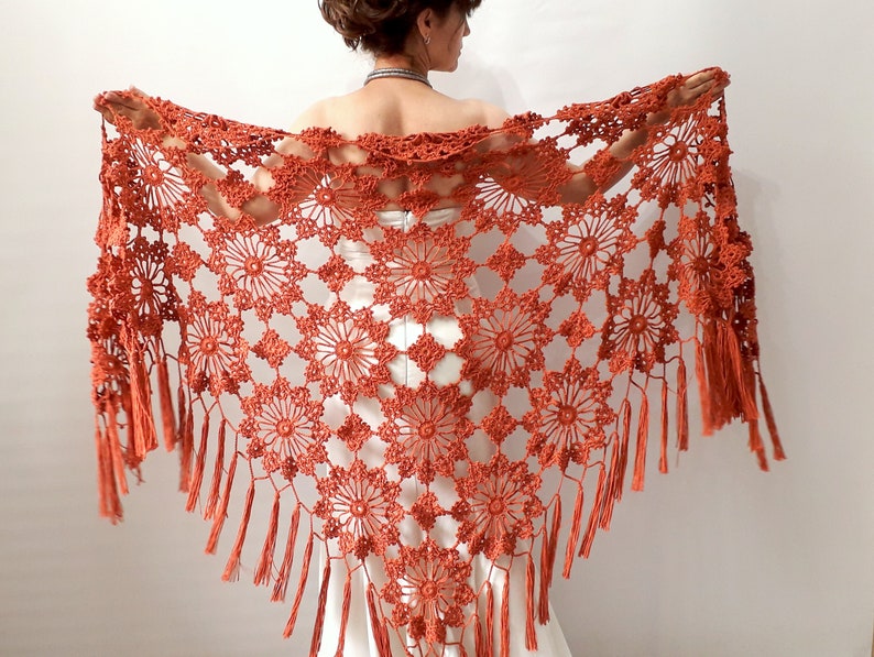 May include: A terracotta crocheted shawl with a fringed border. The shawl is made with a delicate, openwork pattern.