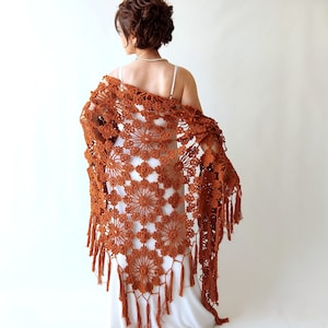 May include: A rust-coloured crocheted shawl with fringe. The shawl is made with a delicate openwork pattern and has a scalloped edge.