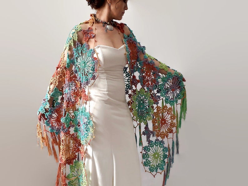 May include: A colorful crochet shawl with a floral pattern and fringe. The shawl is made with a variety of colors, including orange, green, blue, and purple.