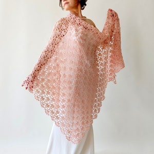 May include: A delicate, crocheted shawl in a soft pink hue. The shawl features a lacy, floral pattern and a triangular shape.