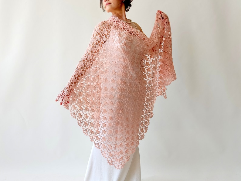 May include: A delicate, crocheted shawl in a soft pink hue. The shawl features a lacy, floral pattern and a triangular shape.