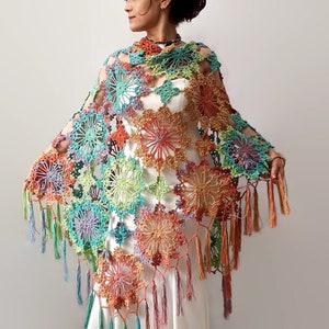 May include: A colorful crochet shawl with a floral design and fringe. The shawl is made with a variety of colors, including green, blue, orange, and pink.