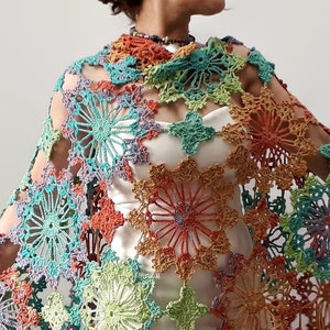May include: A colorful crochet shawl with a geometric pattern of large, open flowers. The shawl is made with a variety of shades of blue, green, orange, and purple yarn.