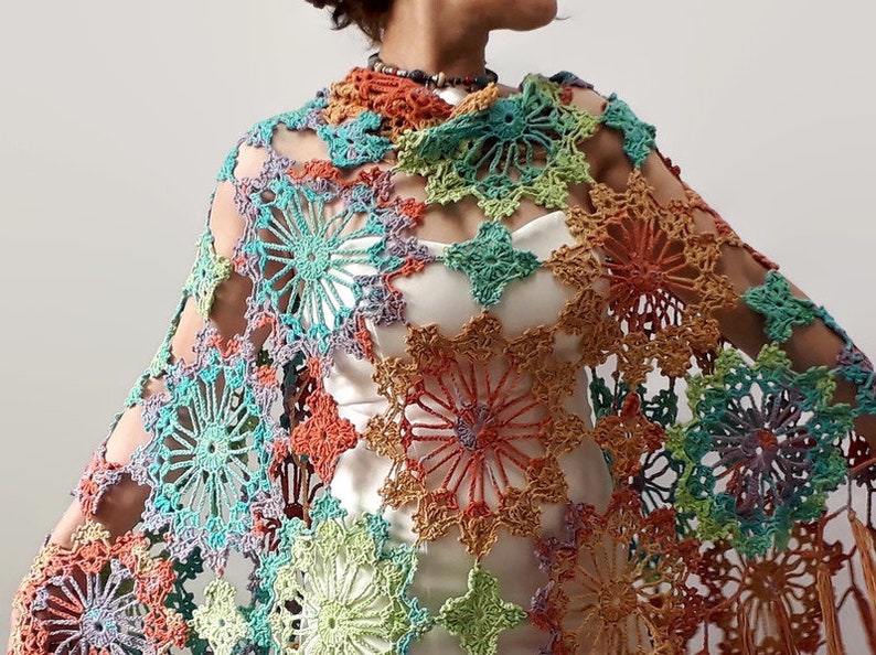 May include: A colorful crochet shawl with a geometric pattern of large, open flowers. The shawl is made with a variety of shades of blue, green, orange, and purple yarn.
