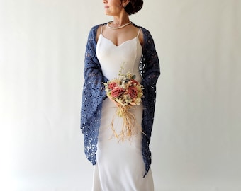May include: A woman wearing a white dress and a blue crocheted shawl holds a bouquet of dried flowers.