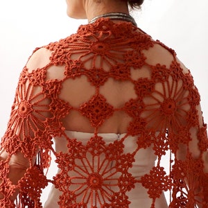 May include: A rust-colored crocheted shawl with a delicate floral pattern. The shawl is made with a lightweight yarn and has a fringed edge.