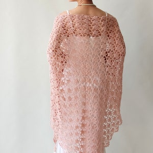May include: A delicate pink crocheted shawl with a lacy pattern. The shawl is draped over a person's shoulders and is a beautiful accessory for any occasion.