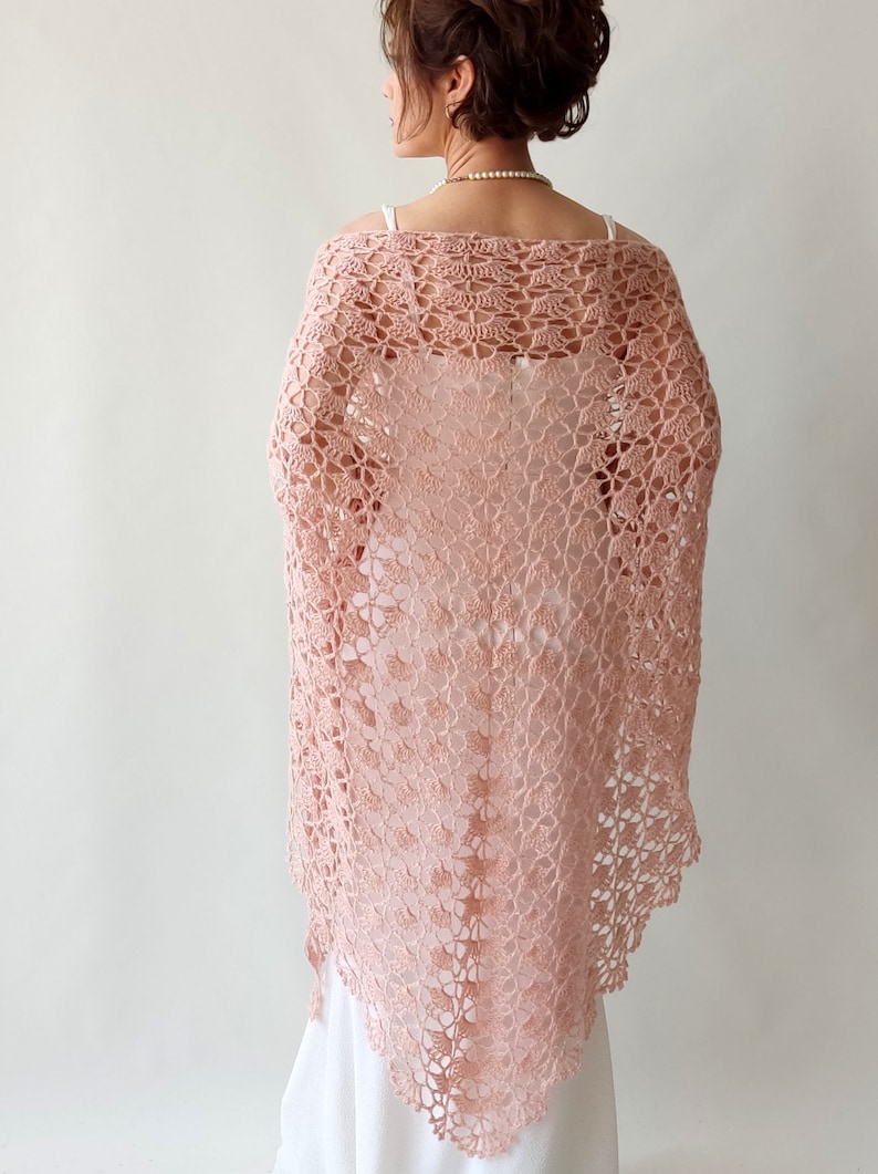 May include: A delicate pink crocheted shawl with a lacy pattern. The shawl is draped over a person's shoulders and is a beautiful accessory for any occasion.