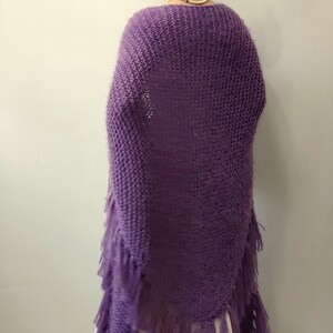 May include: A purple knitted shawl with fringe. The shawl is made of a soft, fuzzy yarn and has a triangular shape.
