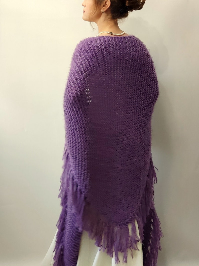 May include: A purple knitted shawl with fringe. The shawl is made of a soft, fuzzy yarn and has a triangular shape.