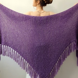 May include: A purple knitted shawl with fringe. The shawl is made of a soft, lightweight yarn and has a delicate, openwork design.