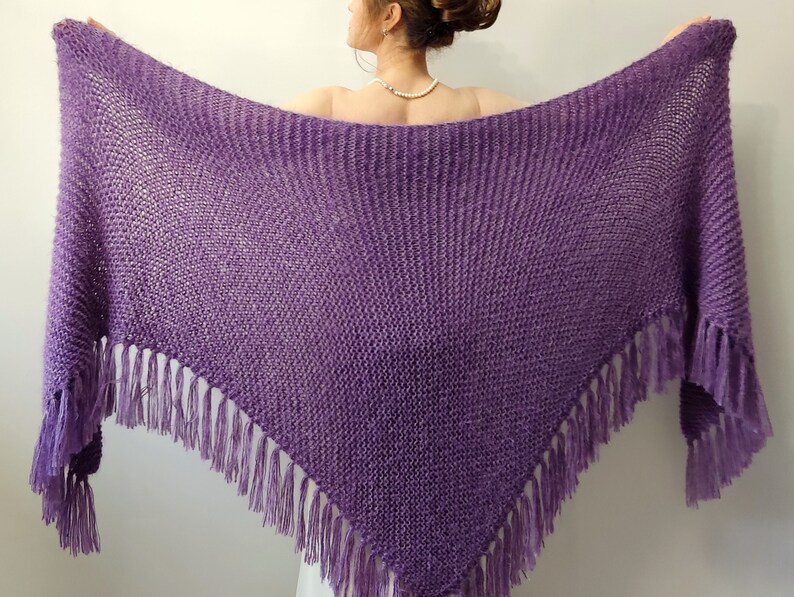 May include: A purple knitted shawl with fringe. The shawl is made of a soft, lightweight yarn and has a delicate, openwork design.