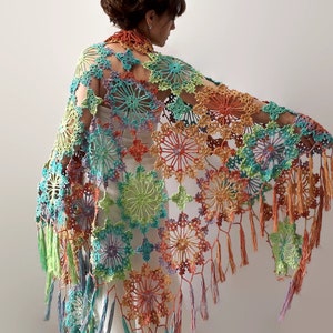 May include: A colorful crochet shawl with a fringed edge. The shawl is made of a variety of colors, including green, blue, orange, and purple. The shawl is crocheted in a delicate pattern with a floral design.