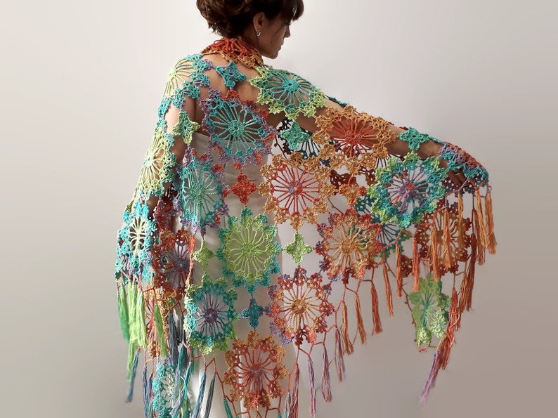 May include: A colorful crochet shawl with a fringed edge. The shawl is made of a variety of colors, including green, blue, orange, and purple. The shawl is crocheted in a delicate pattern with a floral design.