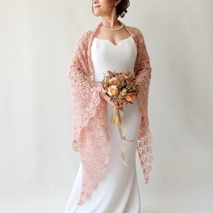 May include: A woman wearing a white dress with a delicate pink crocheted shawl. She is holding a bouquet of dried flowers.