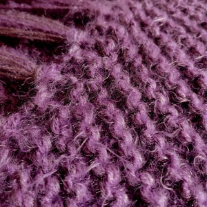 May include: Close-up of a purple fuzzy knitted fabric. The fabric has a soft, fluffy texture and a deep, rich purple color.