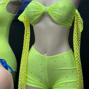 May include: A neon green two-piece outfit with a bandeau top and shorts. The top has a bow detail and both pieces are embellished with rhinestones. The outfit has mesh sleeves.