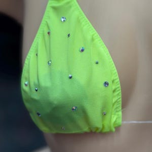 Op de afbeelding: Een neon groene bikini top met doorzichtige bandjes en strass.