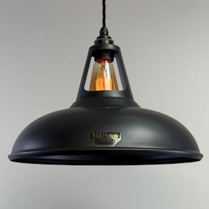 May include: A black metal pendant light with a dome-shaped shade and a visible Edison-style bulb. The light fixture has a vintage industrial design, with the word "BENJAMIN" on a small label. The light hangs from a black cord.